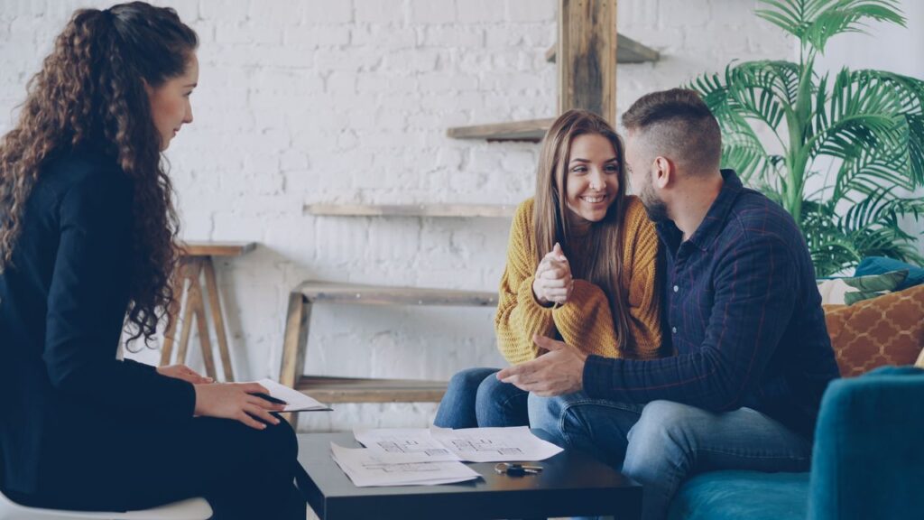 Smiling couple discussing real estate plans with advisor in modern, cozy setting.