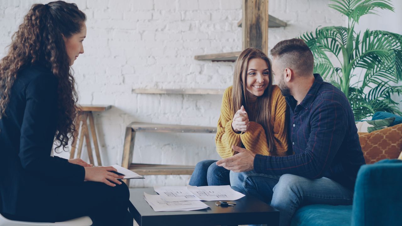 Smiling couple discussing real estate plans with advisor in modern, cozy setting.